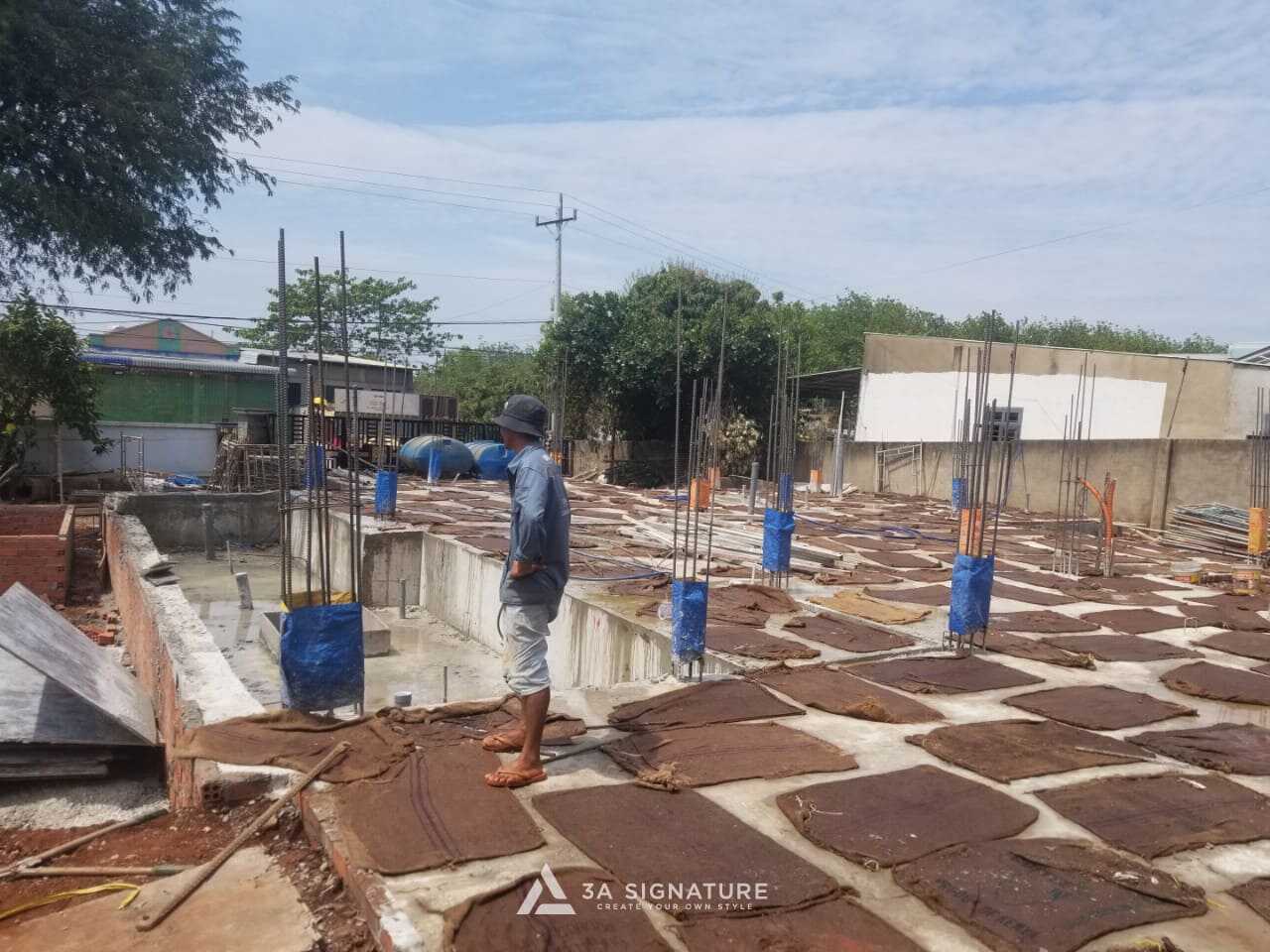 Thi Công Biệt Thự Green Villa – Giai Đoạn Đổ Bê Tông Móng Chuẩn Kỹ Thuật Người công nhân kiểm tra công trình móng vừa đổ bê tông, bề mặt đã được phủ bao tải ẩm để giữ ẩm và bảo dưỡng bê tông trong điều kiện nắng nóng.