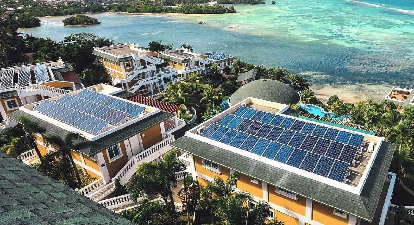 Aerial view of modern tropical villas by the sea equipped with rooftop solar panels, showcasing 3A Signature’s sustainable solar villa design concept.